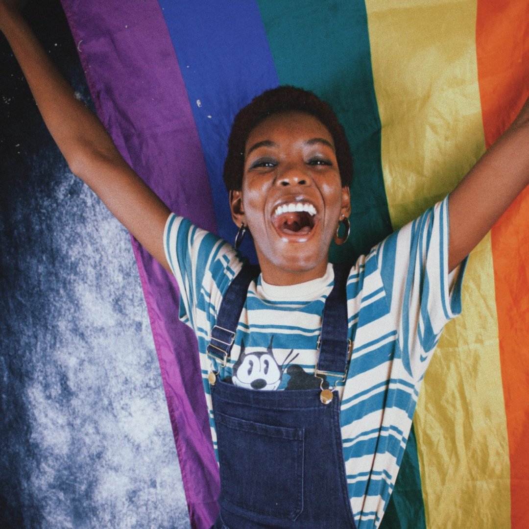 Black woman smiles while holding a rainbow flag