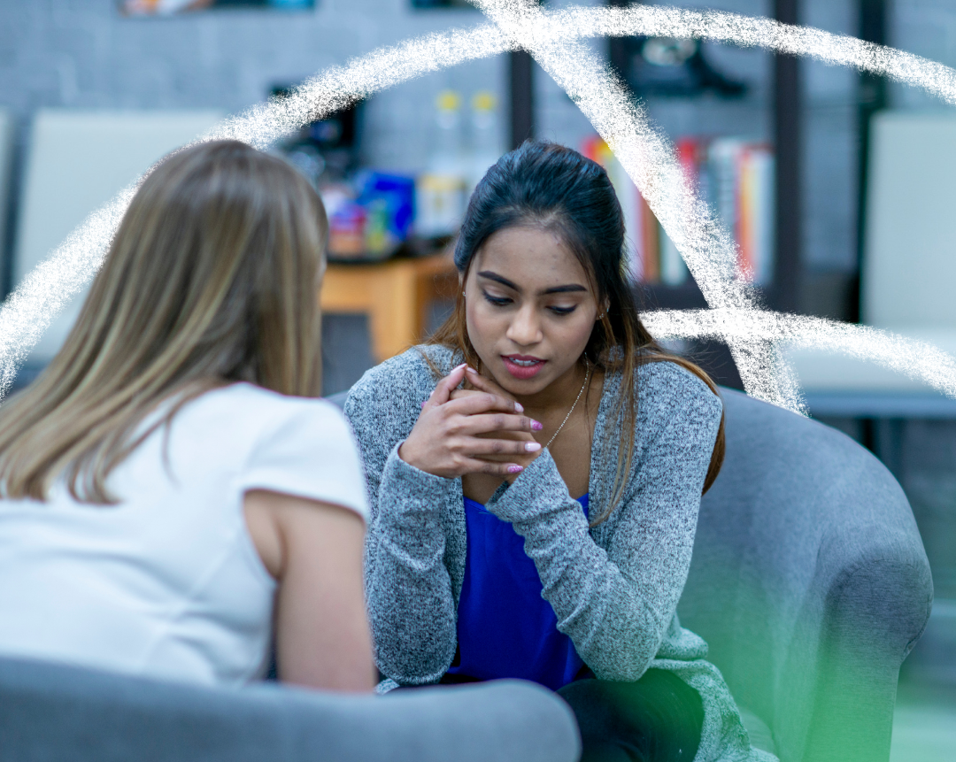 two women sitting in armchairs talking. one woman has her eyes downcast and looks troubled