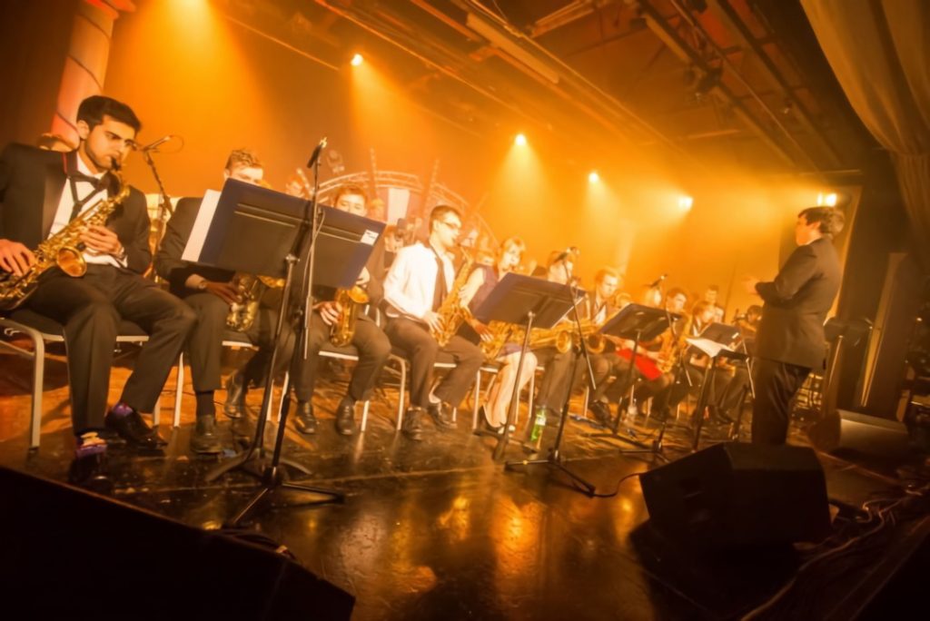 An orchestra group plays on a stage that is lit by orange light