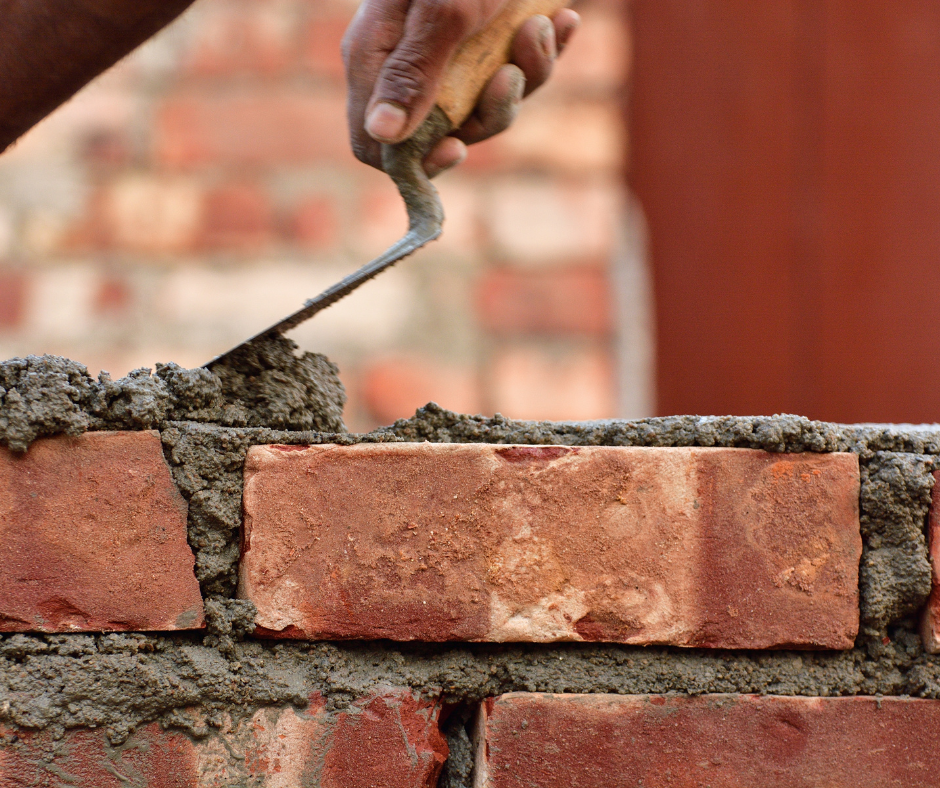A hand is putting cement onto a brick wall