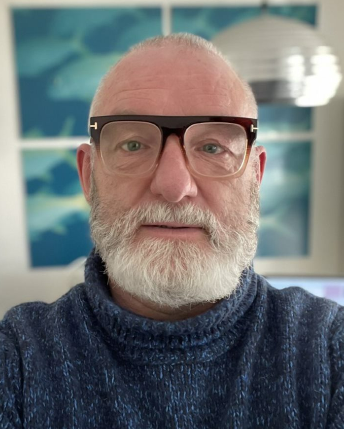 A portrait of a white man with a white beard and black framed glasses.