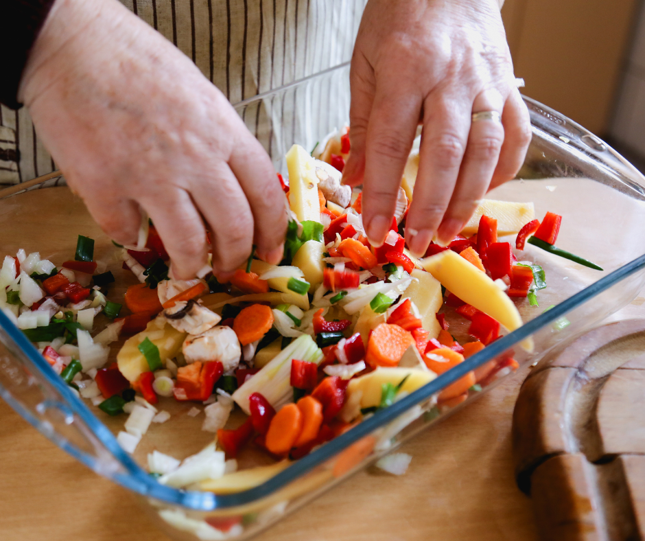 Hands mixing vegetables in a baking dish