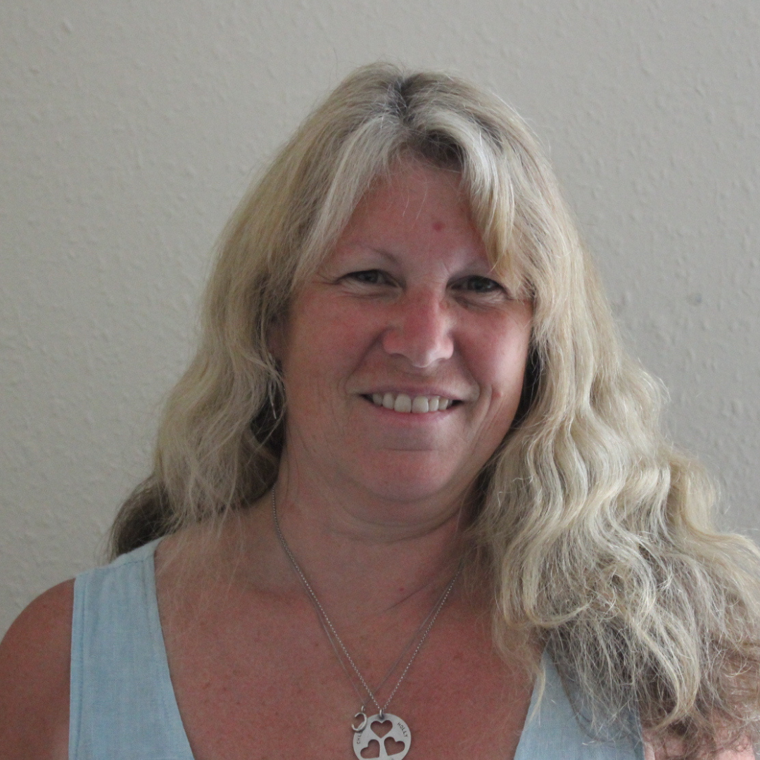 A portrait of a smiling white woman with wavy blonde hair and wearing a blue vest.