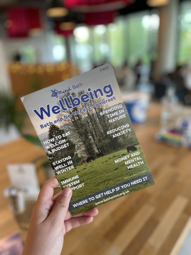 A hand holds up Bath Mind's wellbeing magazines