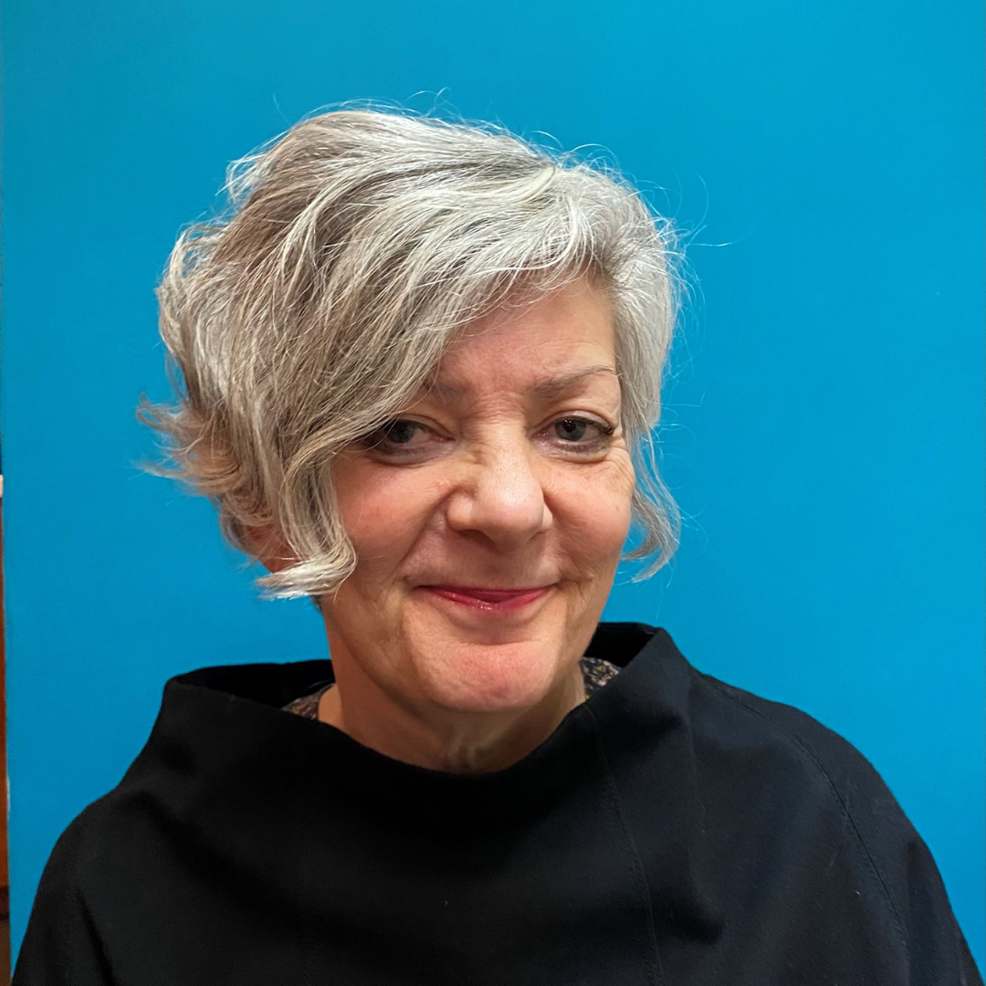A portrait of a white woman with white hearing and wearing a black top smiling