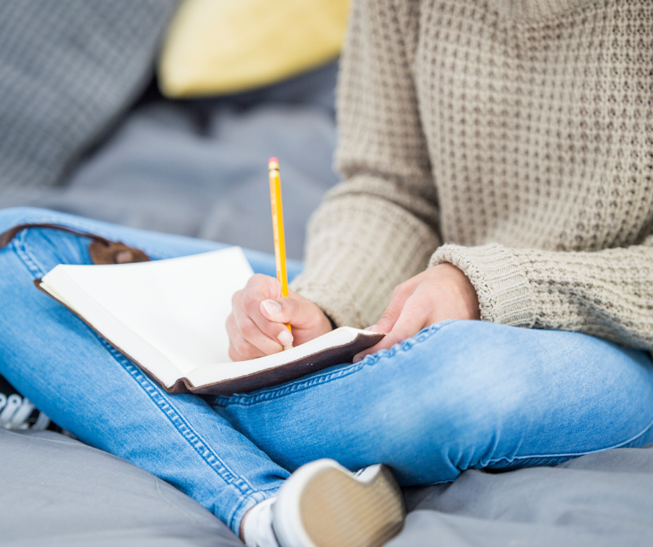 Someone sits cross legged on the floor writing in a notebook