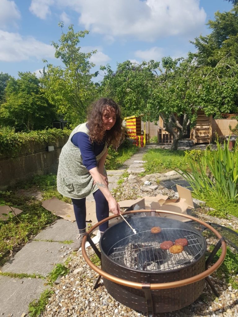 A woman leans over a fire pit cooking BBQ food.