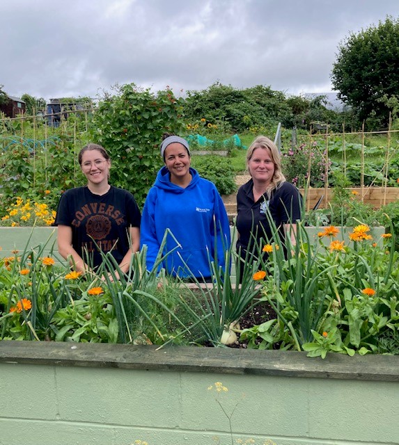 Three women stand in an allotments smiling