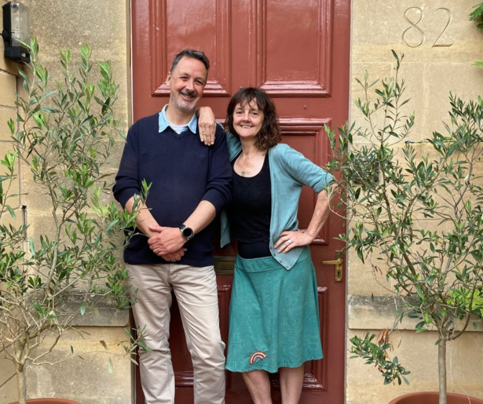 A man and woman stand smiling outside of a house