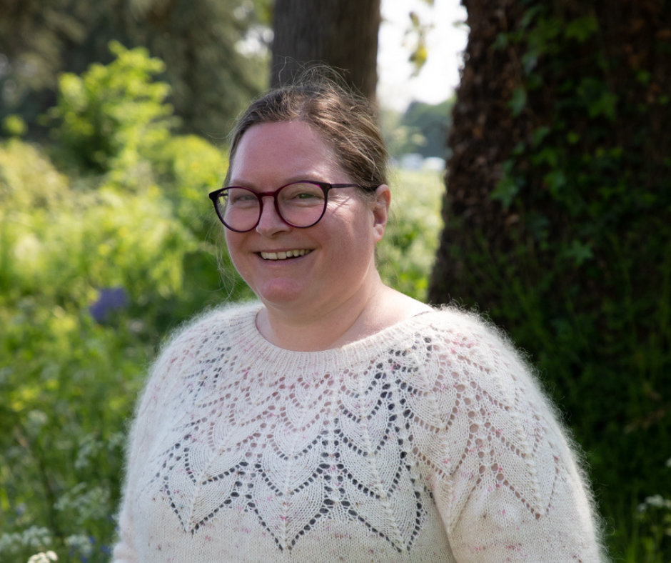 A white woman wearing glasses and a cream coloured jumper is smiling