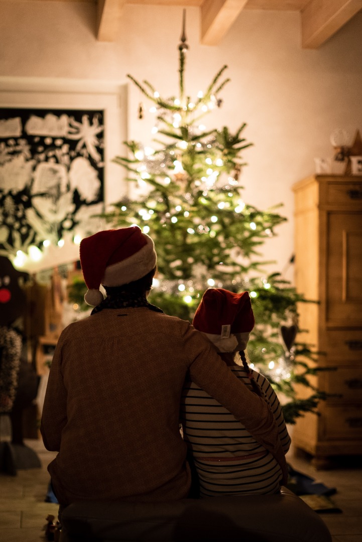 Two people sit facing a Christmas tree snuggled up