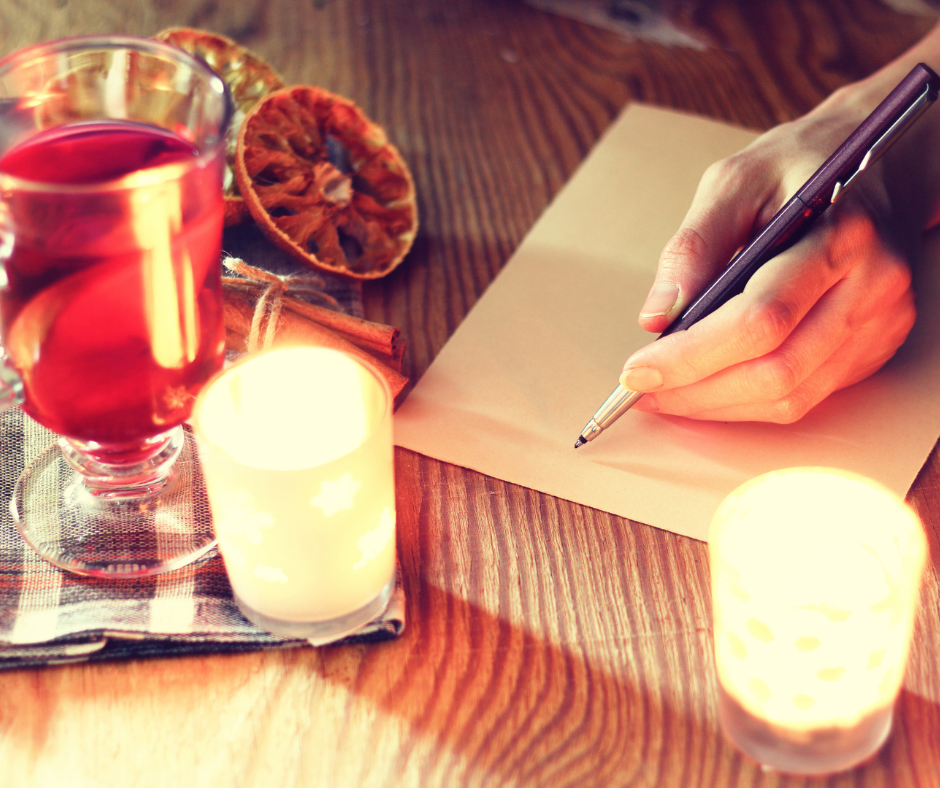 A hand writing on paper surrounded by candles and mulled wine.