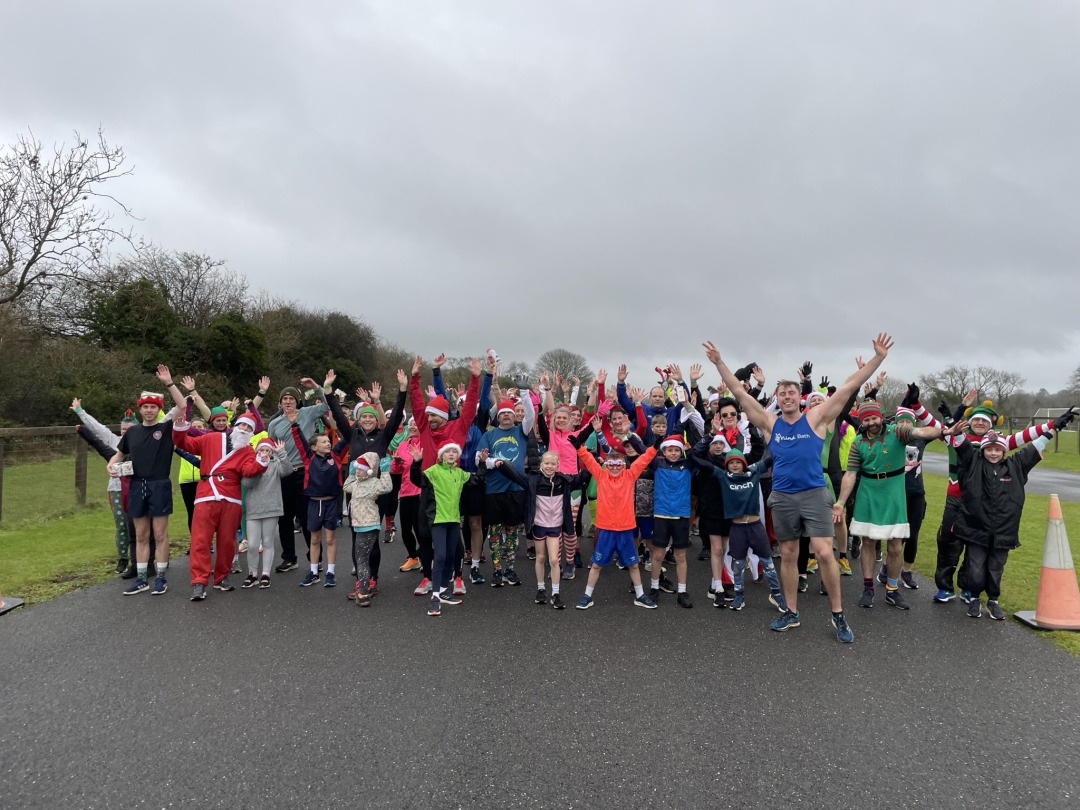 A group of runners in festive gear stand at a race start lane with their hands in the air