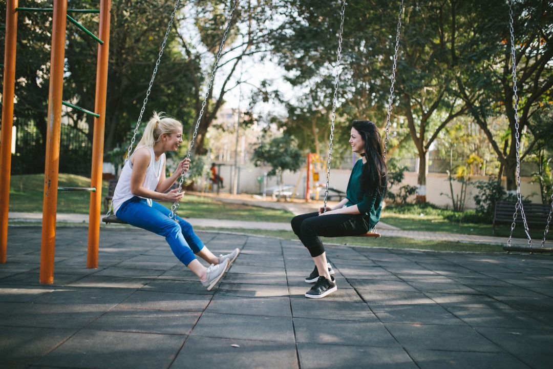 Two women sit on swings facing each other