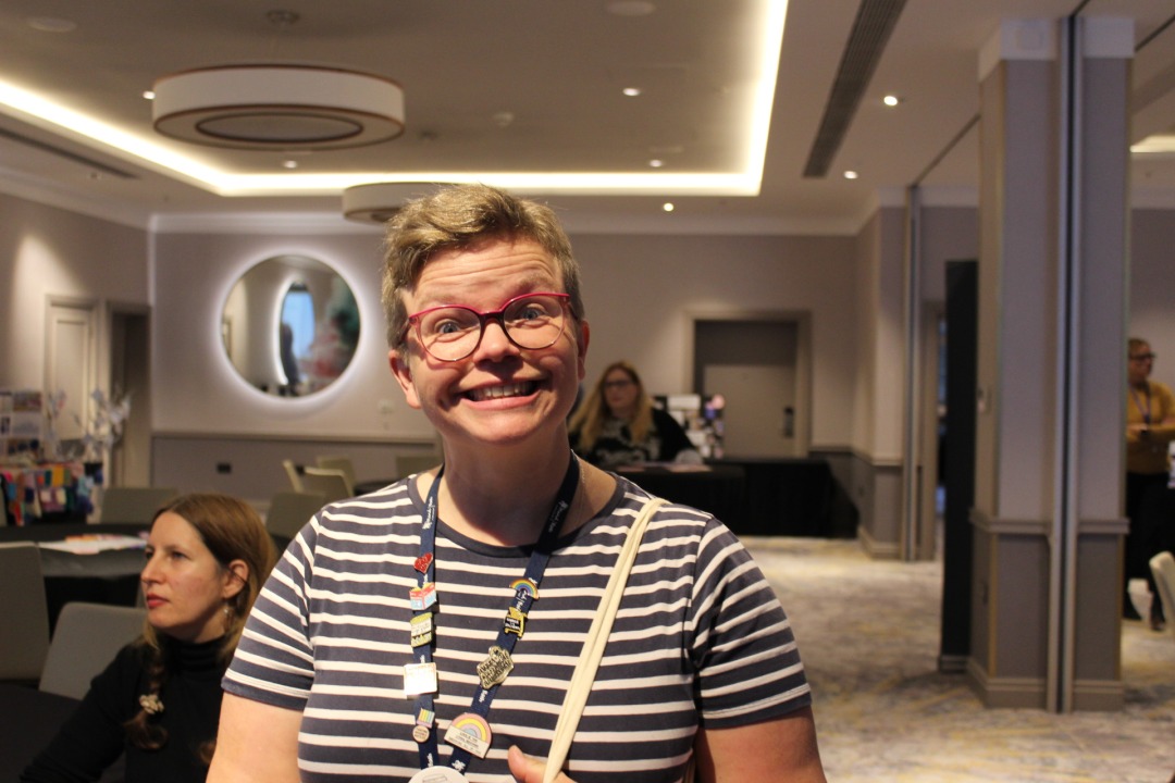 A white woman with short blonde hair and glasses smiles into the camera