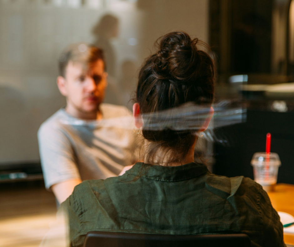 A woman sits opposite a man. They are in a serious looking discussion.