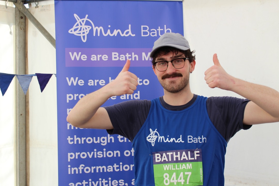A runner wearing a Bath Mind vest smiles proudly after completing a half marathon