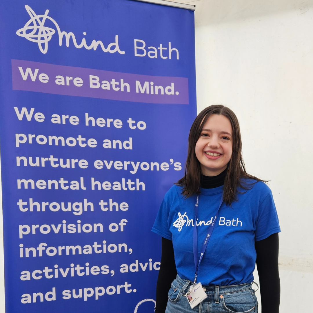 A woman with brown hair stands in front of a Bath Mind banner smiling