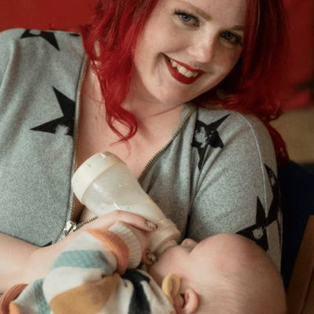 A red haired woman feeding a baby from a bottle