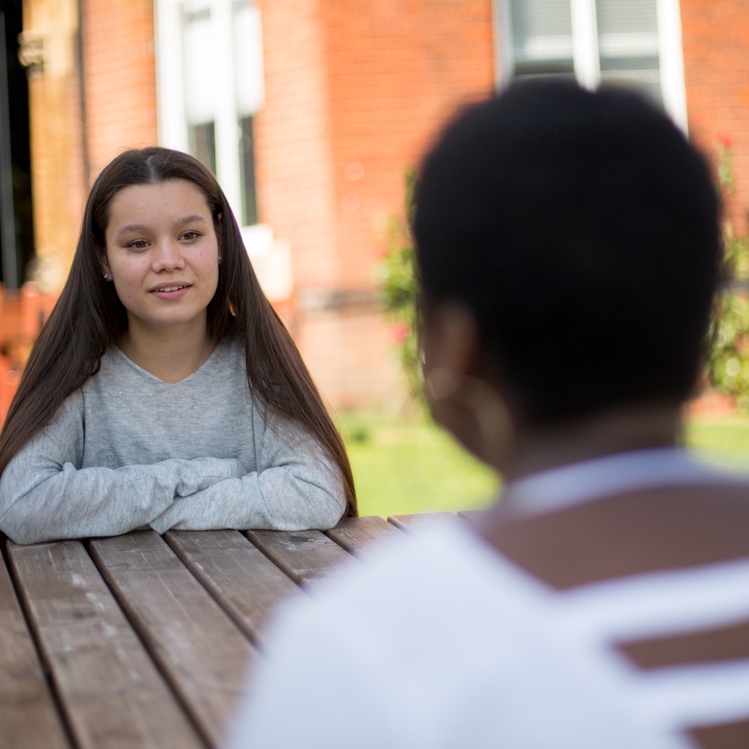 Two young people talking at a bench outside