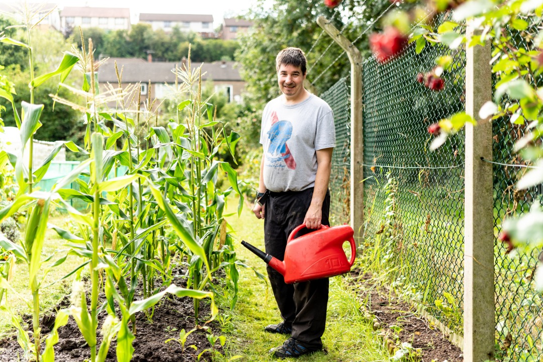 A man in an allotment holding a watering can