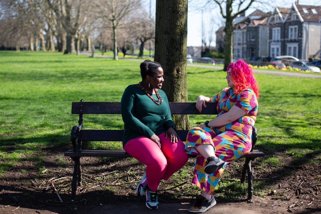 Two people talking on a bench in a park