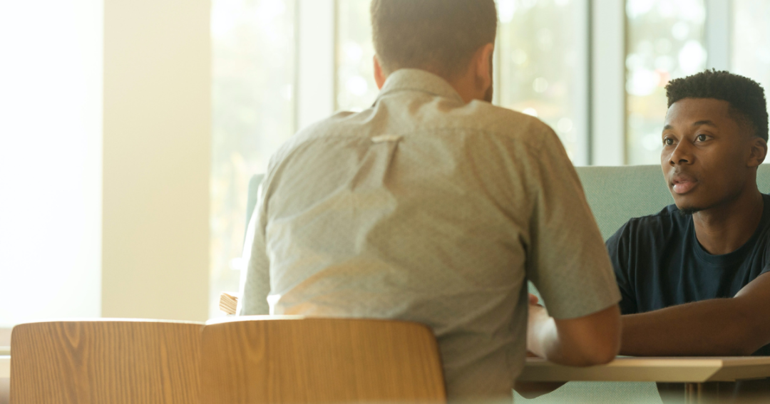 two men talking to each other over a table