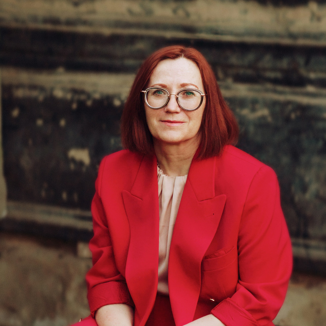 A woman wearing a red blazer and glasses.