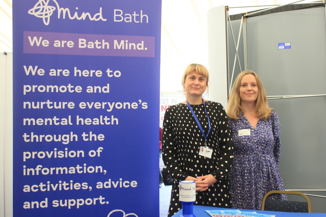 Two Bath Mind staff by a banner