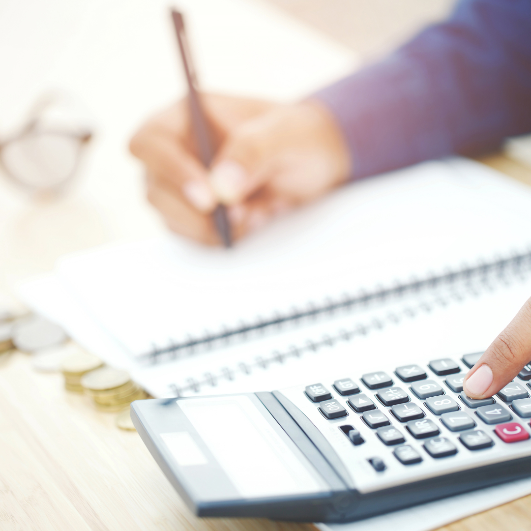 a person writing in a notepad and typing on a calculator